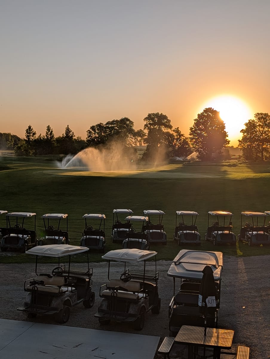 Sunset over the course with sprinklers running and carts parked nearby